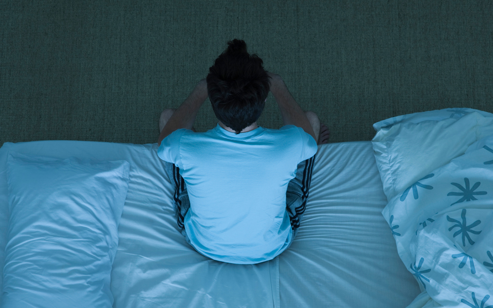 A man on the edge of his bed who can't sleep fighting insomnia because of anxiety.